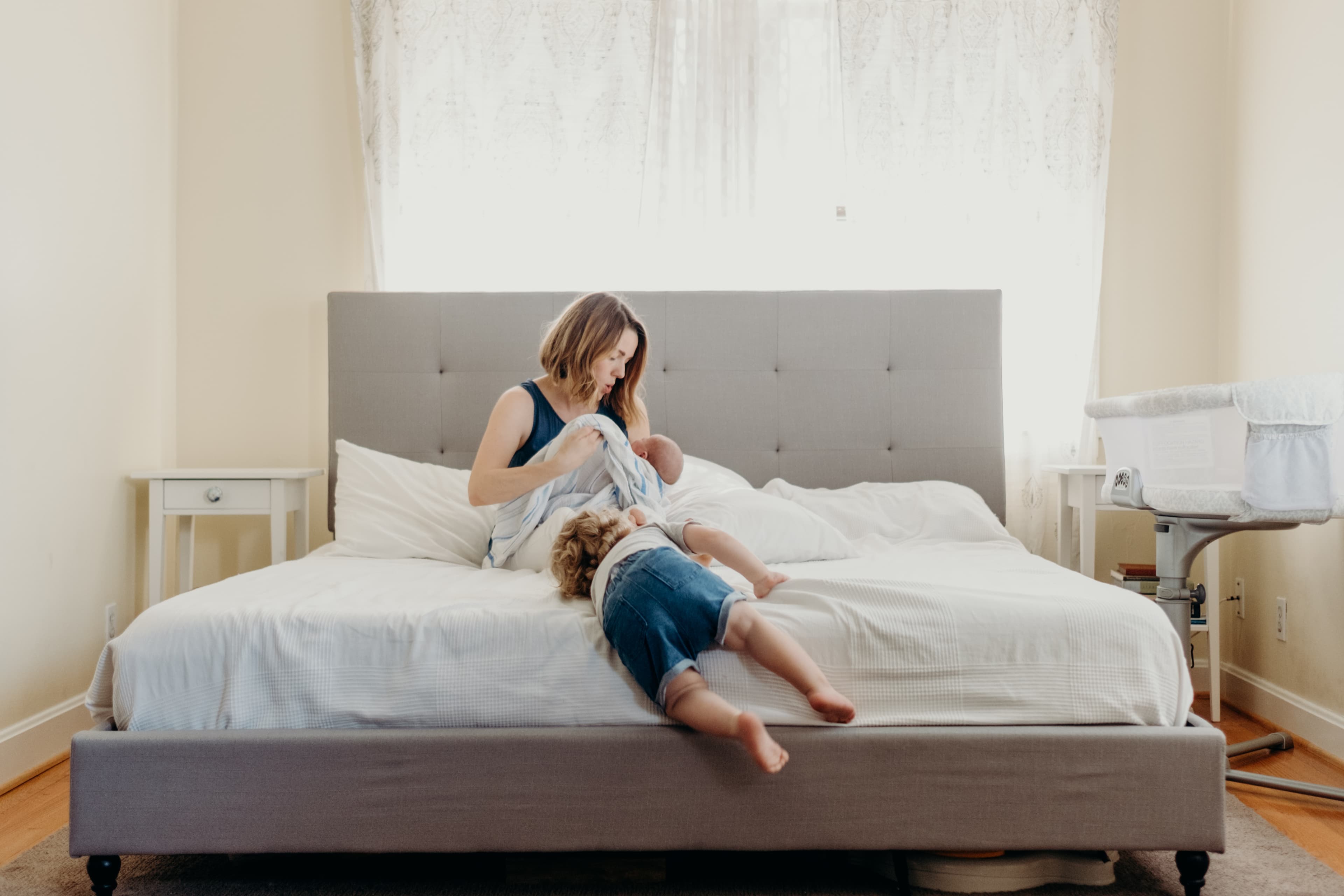 A mother cradling her newborn on the bed while her toddler nestles beside her